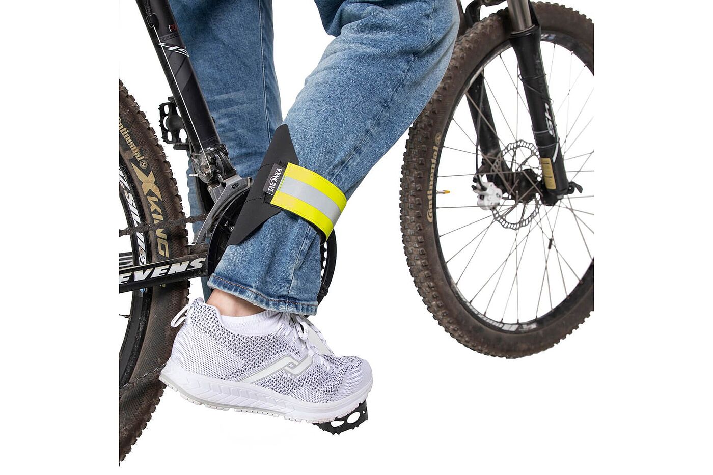 Ein Hosenbein wird beim Radfahren mit einem gelb reflektierenden Klettband am Bein fixiert; zu sehen sind das Fahrrad und der Fuß auf dem Pedal.